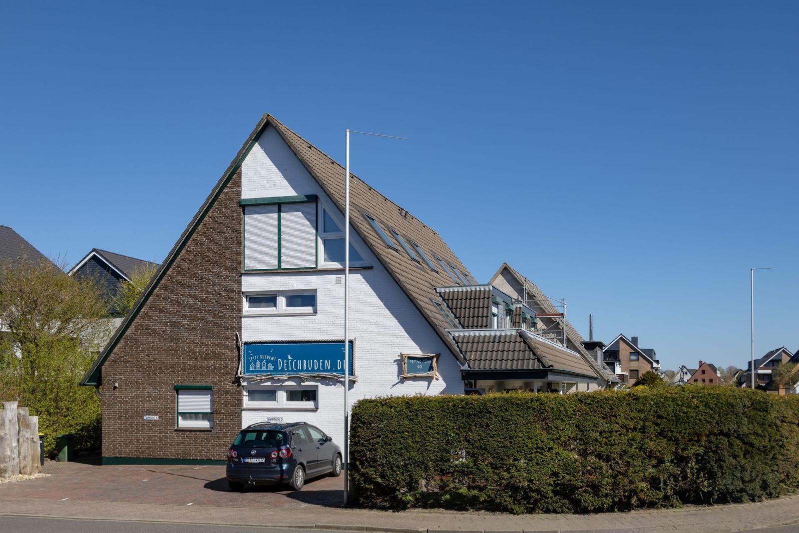 Ein zweistöckiges Haus mit braunem und weißem Putz, Dachfenstern und einem Parkplatz vorne.