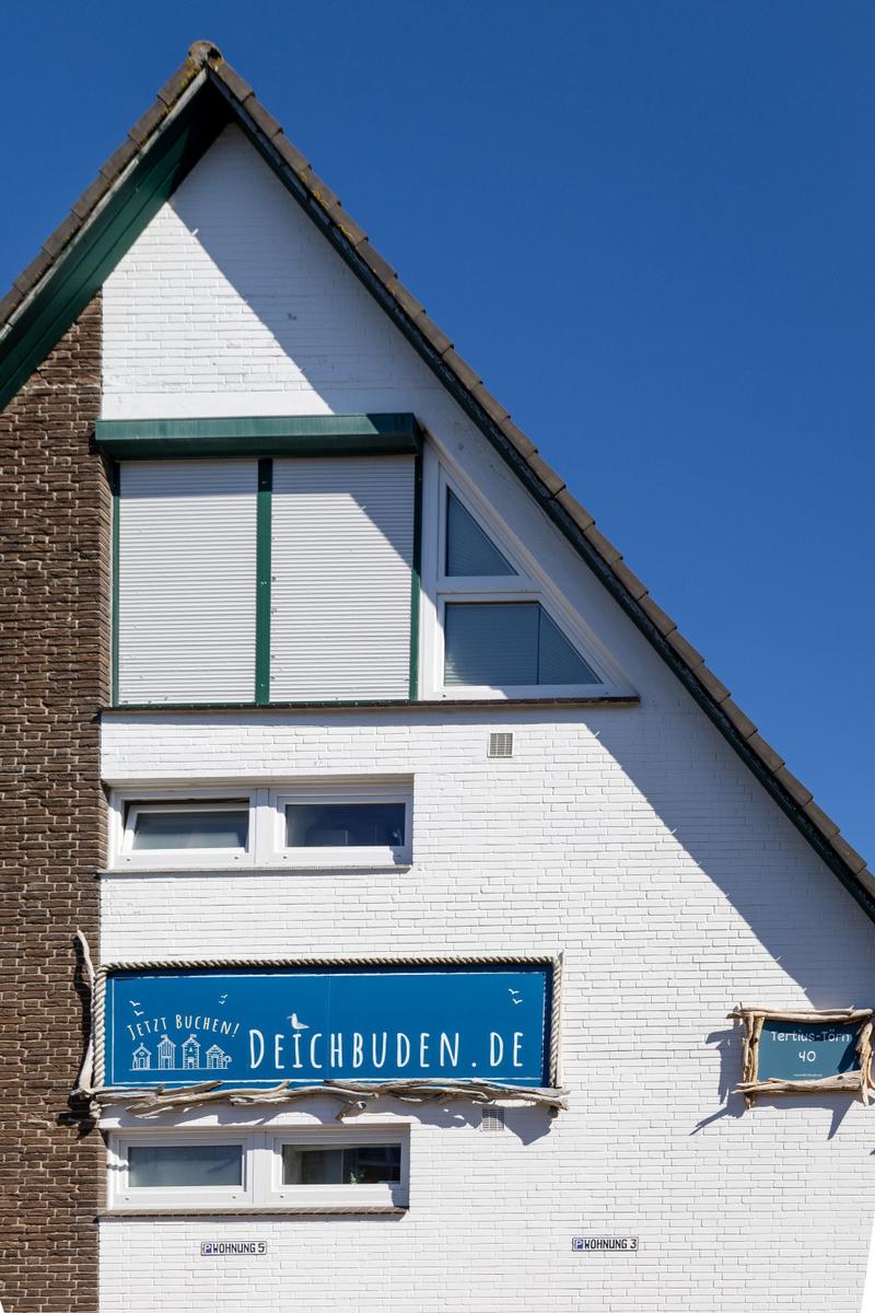 Ferienhaus mit weißen Wänden und blauem Schild. Fenster und Dach sind sichtbar.