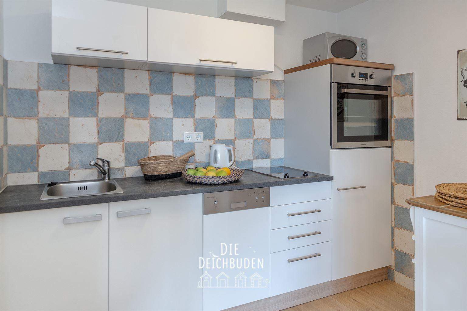 Küche mit Spüle, Herd, Backofen und Kühlschrank. Fliesenwand und Holzboden.