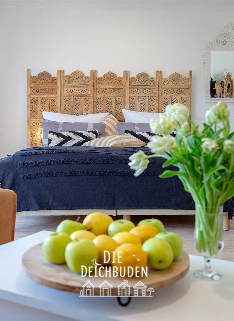Schlafzimmer mit Holzbett und Blumen. Obst auf Tisch im Vordergrund.