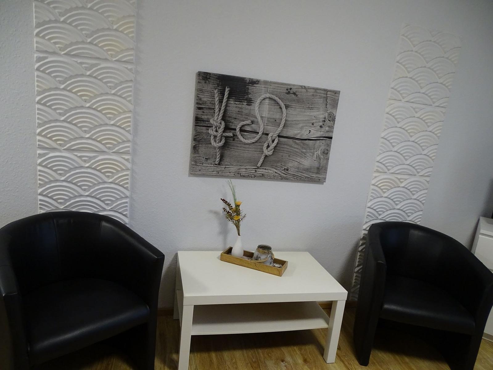Zwei schwarze Sessel stehen um einen weißen Tisch herum. An der Wand hängt ein Bild mit Seil.