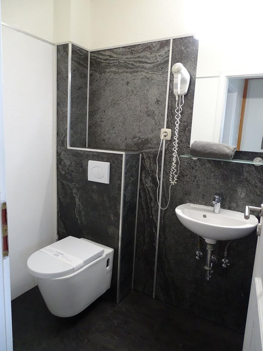 Bad mit Toilette, Waschbecken und Handtuchhalter an grauem Steinwand