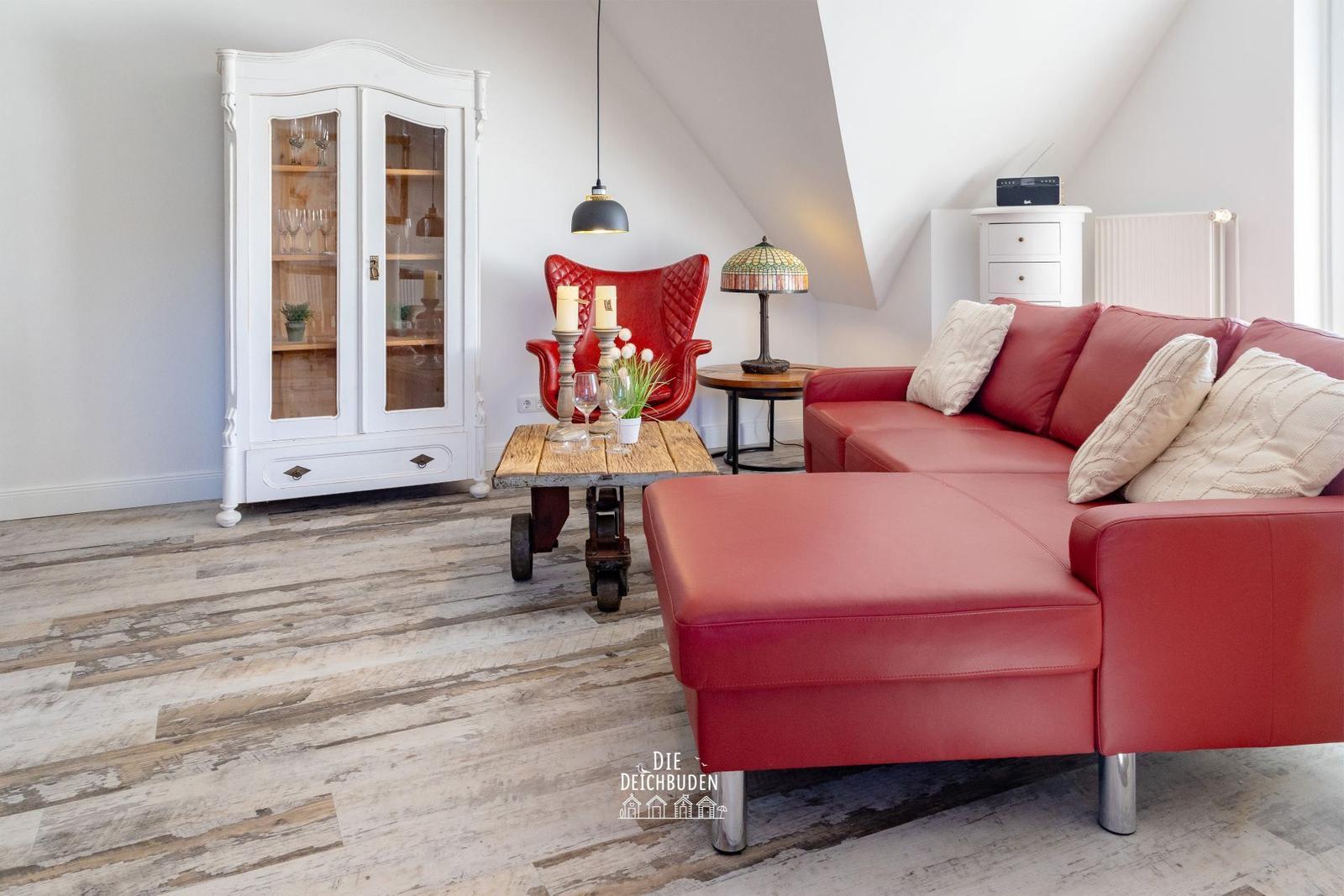 Rotes Sofa, weiße Schrank, Holzboden und Sessel im Wohnzimmer.