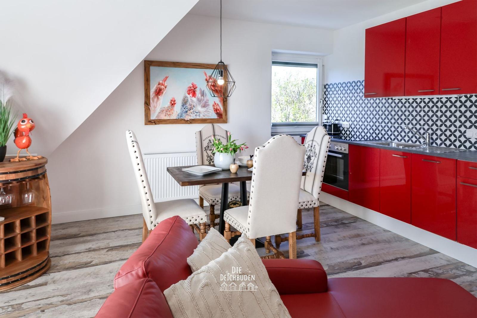 Essbereich mit rotem Sofa, Esstisch und roter Küche unter Dachschrägen.