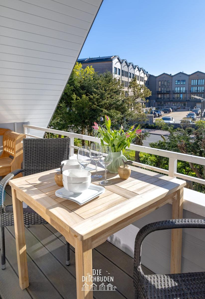 Terrasse mit Tisch, Stühlen und Blumen. Blick auf Wohngebäude und Bäume.