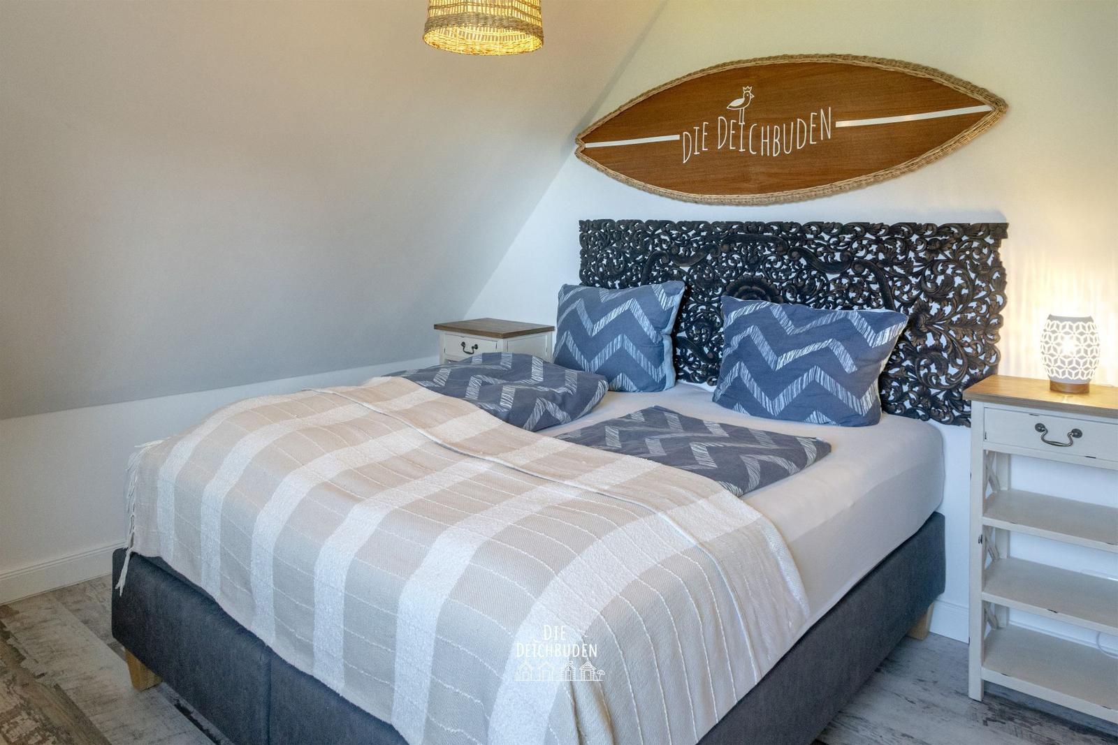 Schlafzimmer mit Bett, Nachttischen und Surfbrett an der Wand.