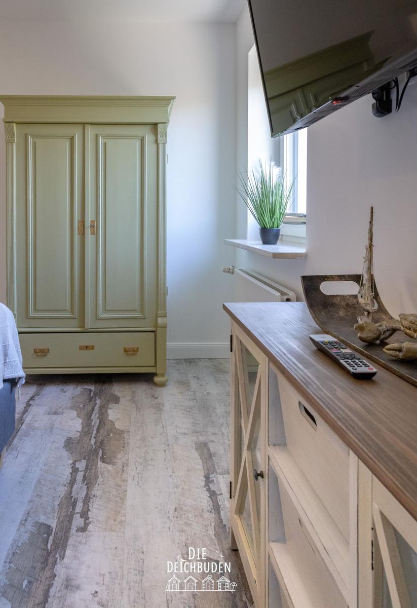 Schlafzimmer mit grünem Schrank, Holzboden und TV über dem Schrank.