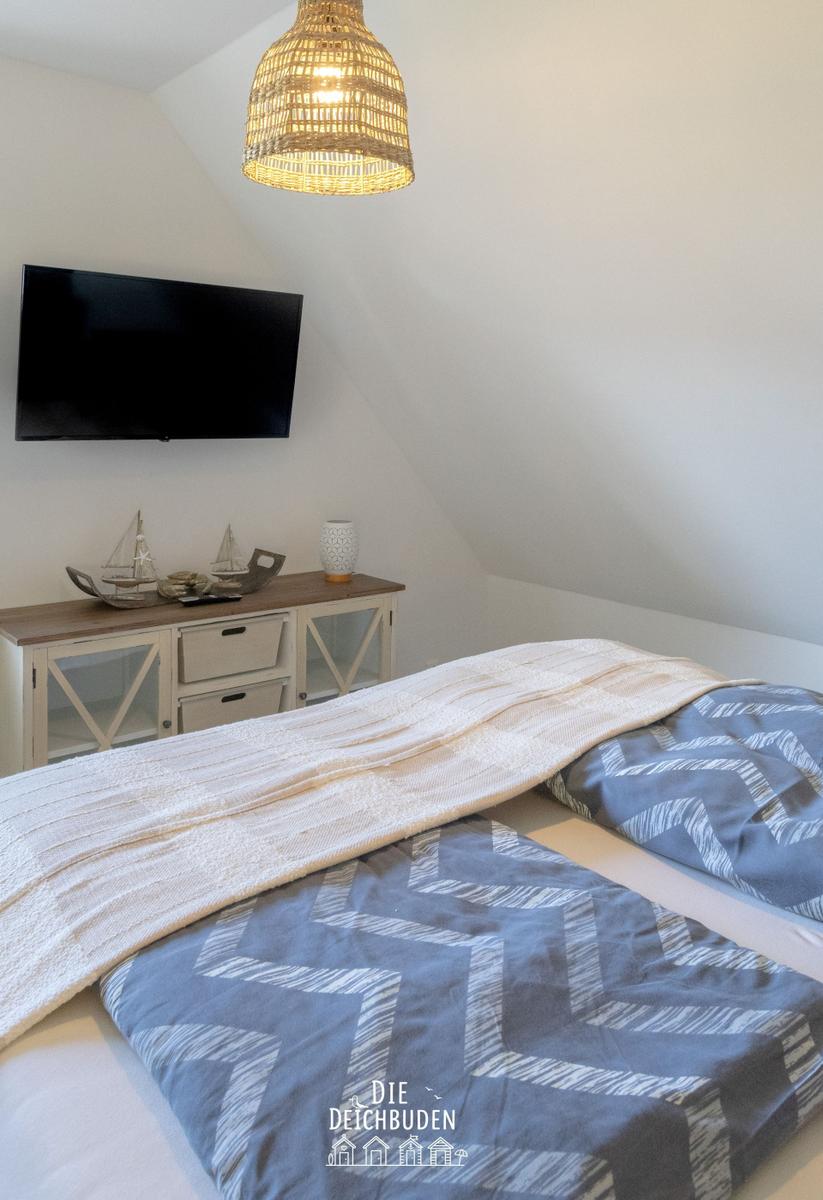 Schlafzimmer mit Dachschräge, Bett mit gemustertem Bettbezug, TV und Schrank.