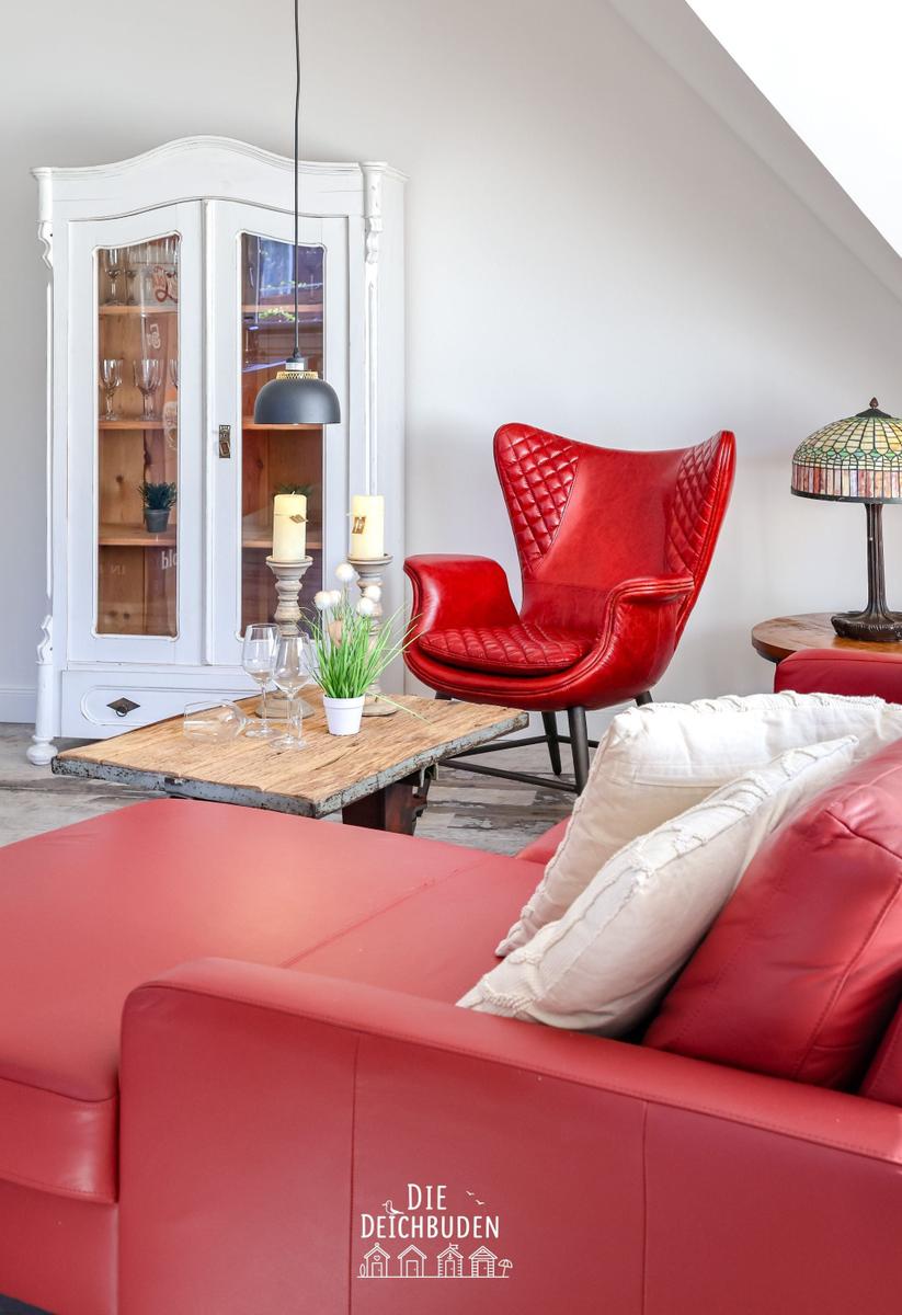 Ein Wohnzimmer mit rotem Sofa, rotem Sessel und weißem Schrank.