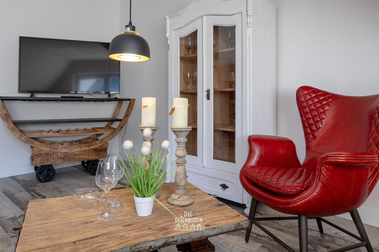 Ein Wohnzimmer mit rotem Ledersessel, Holztisch und Fernseher auf rustikalem Gestell.