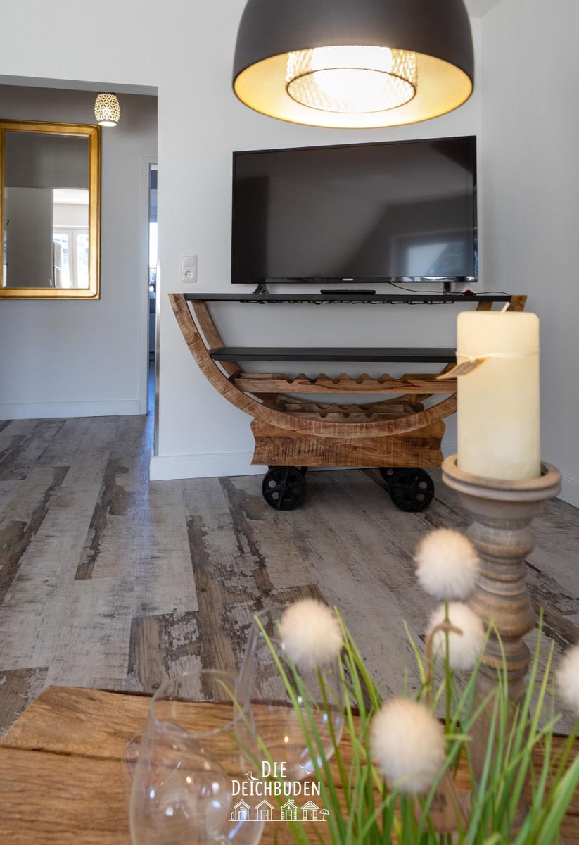 TV auf Holzregal mit Rollen, große Deckenlampe und Kerze auf Tisch