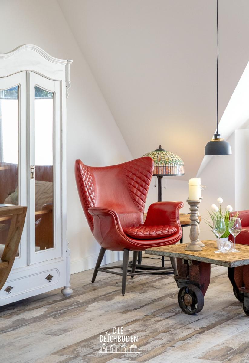 Rotes Ledersofa, Holztisch und weißer Schrank im Dachbodenraum mit Holzboden und Lampen.
