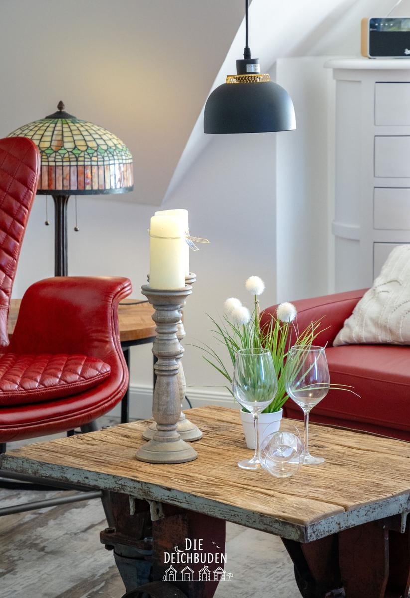 Eckzimmer mit rotem Ledersofa, Holztisch und Pendelleuchte.