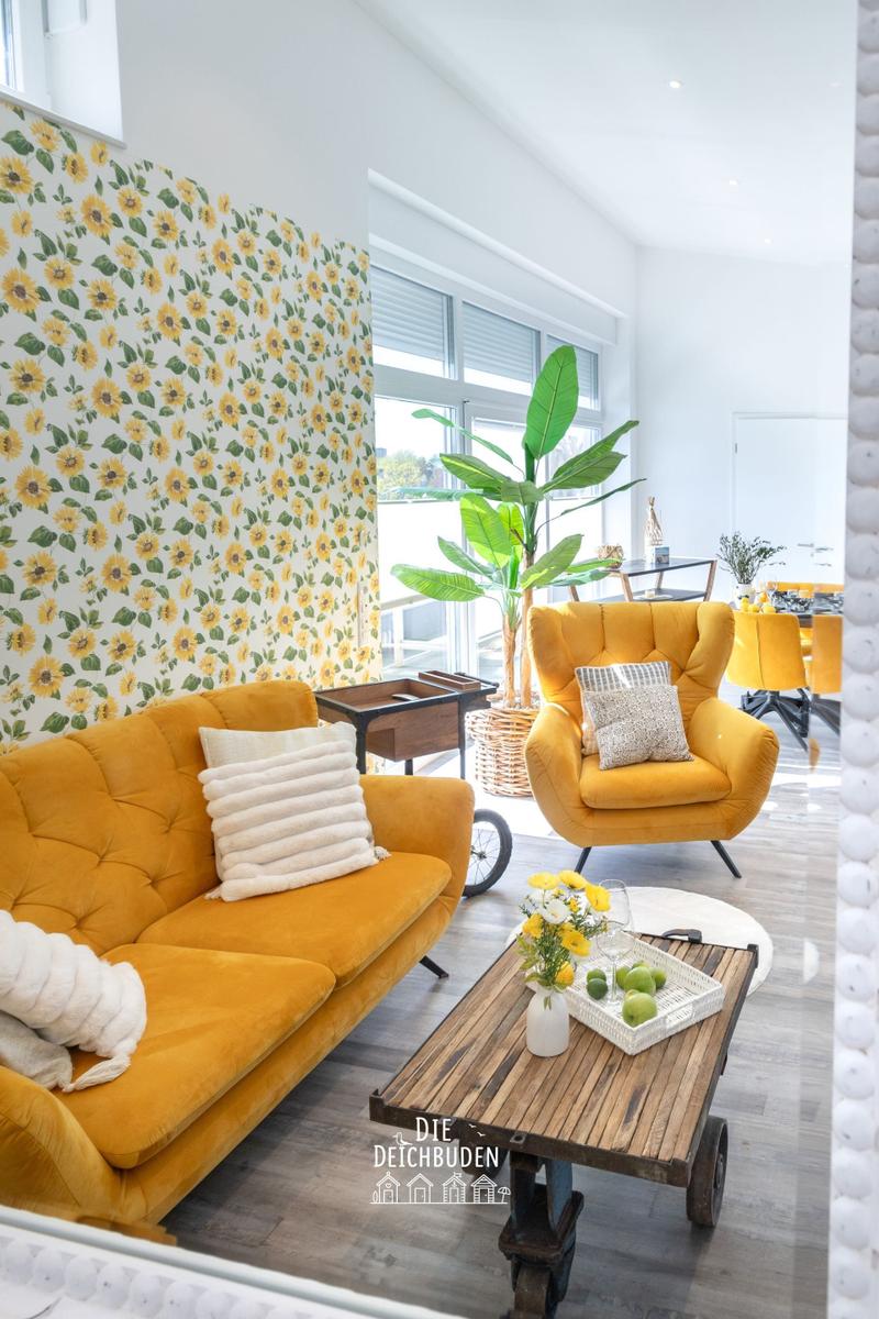 Wohnzimmer mit gelbem Sofa, Sonnenblumenwand und Holztablett.