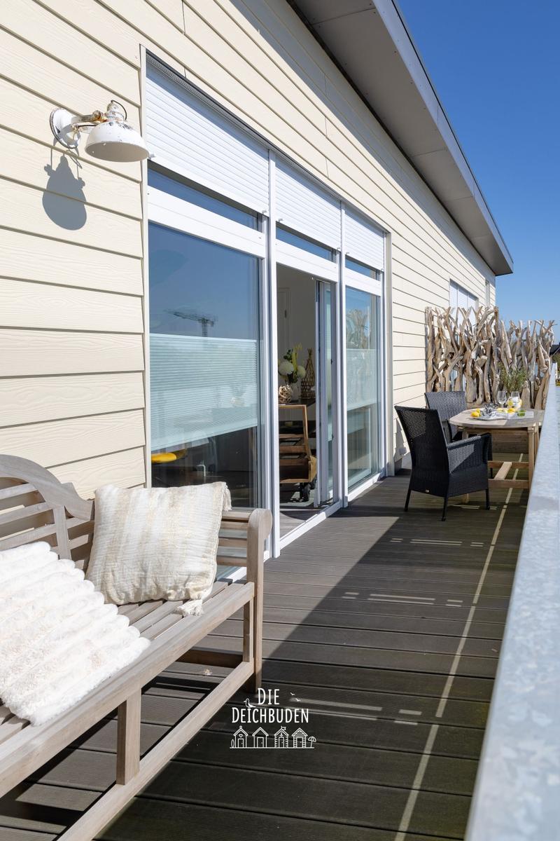 Terrasse mit Holzbank, Tisch und Stühlen. Große Fenster zur Aussicht.