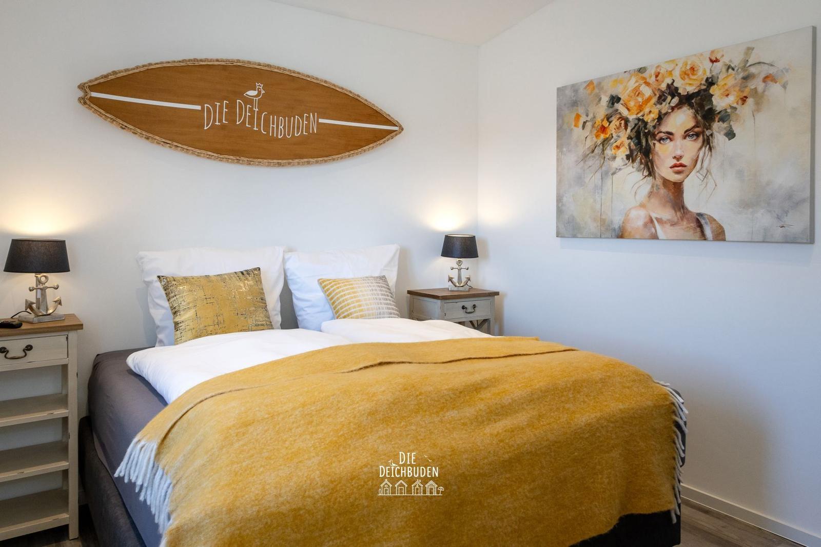 Schlafzimmer mit Bett, Nachttischen und Wandbild. Decke und Kissen sind gelb.