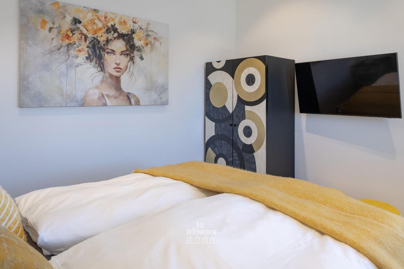 Schlafzimmer mit Bett, Wandbild, Schrank und Fernseher.