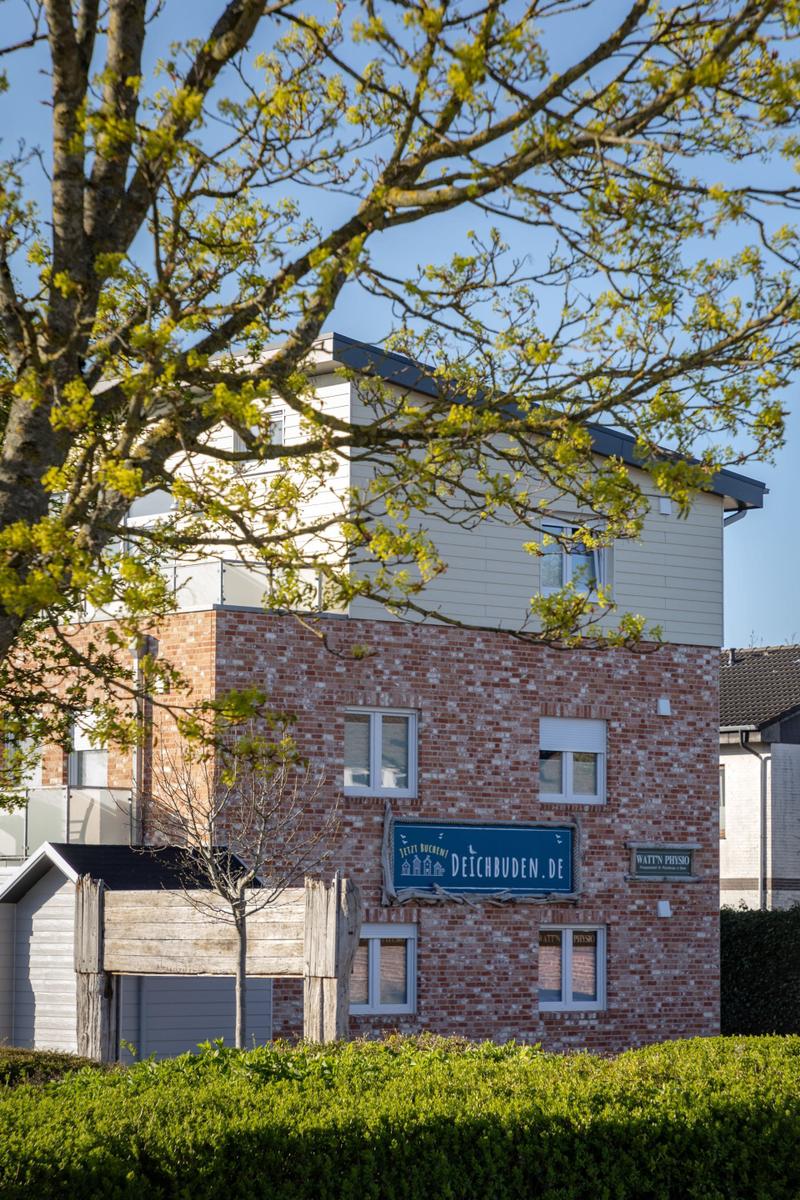 Zweistöckiges Haus mit Backsteinfassade und Schild. Blick durch Baumzweige.