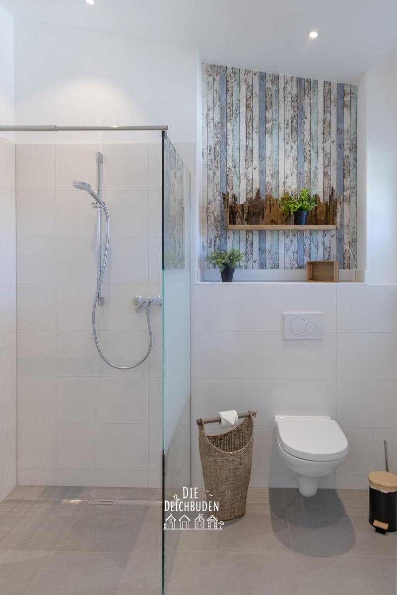 Dusche mit Glaswand, Toilette und Holzwand mit Pflanzen.