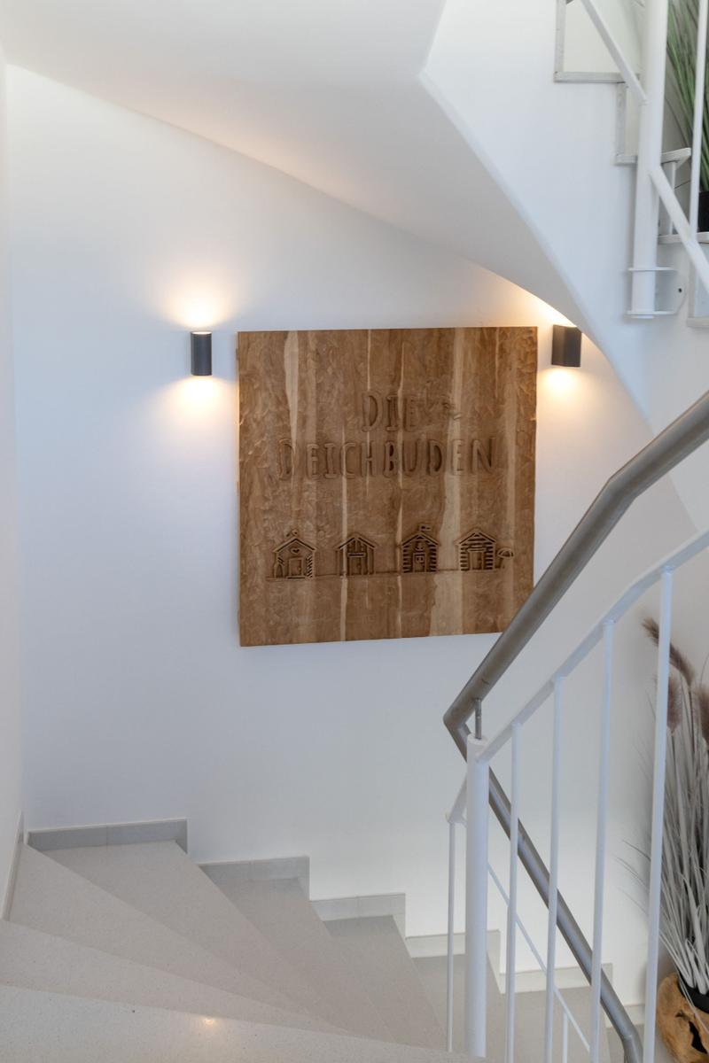 Holzschild mit Namen an Wand neben Treppe mit Metallgeländer