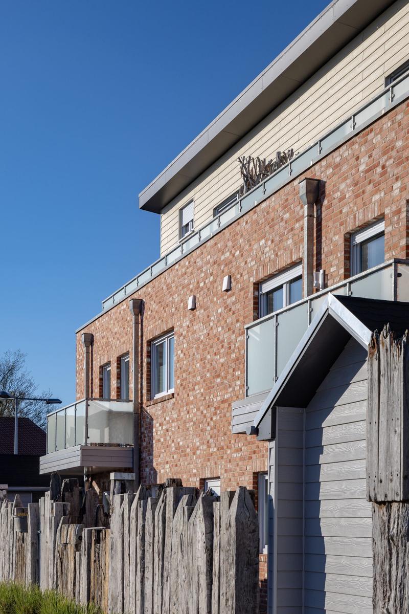 Modernes Haus mit Backsteinfassade und Glasgeländern an Balkonen unter blauem Himmel.