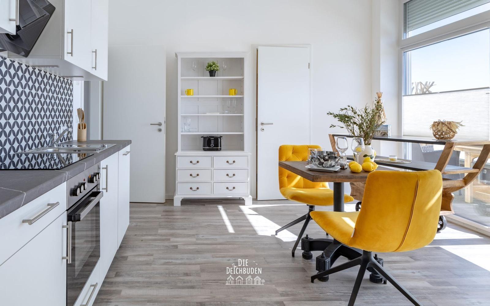 Küche mit Essbereich, gelbe Stühle, weißer Sideboard und großes Fenster.