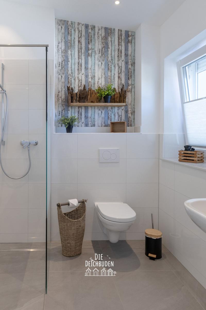 Bad mit Dusche, Toilette und Waschbecken. Wand mit Holzoptik und Pflanzen.