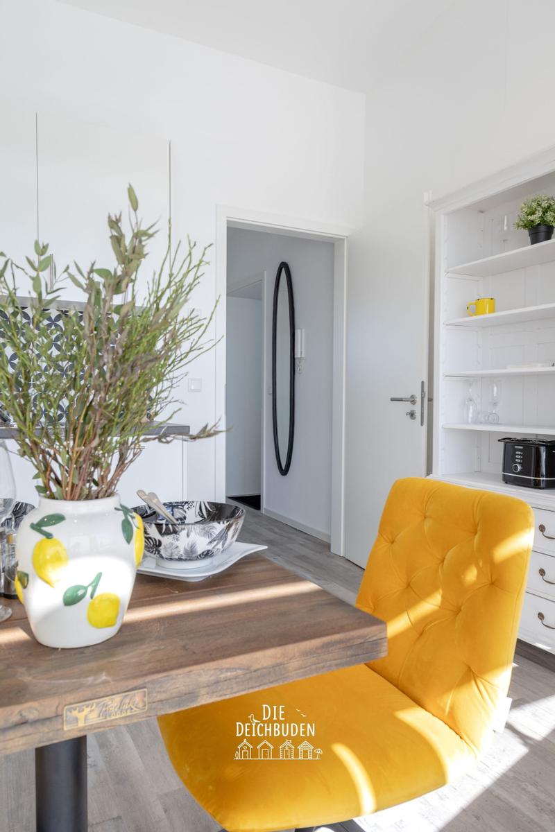 Essbereich mit gelber Stuhllehne, Holztisch und Pflanze im Vase.