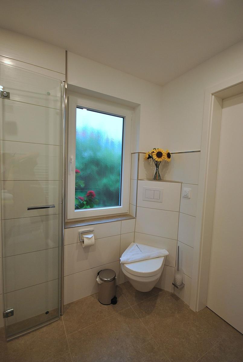 Badezimmer mit Dusche, Toilette und Fenster mit Sonnenblumen.