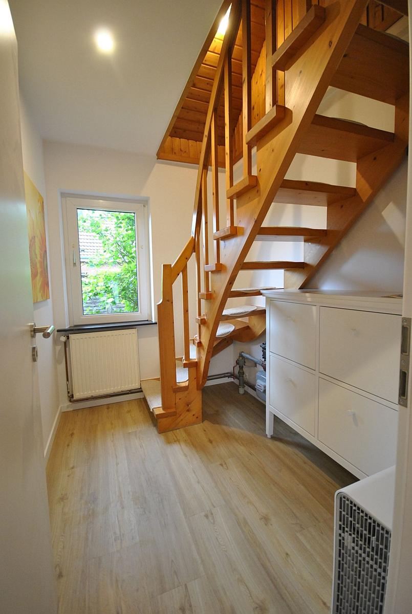 Holztreppe führt nach oben, daneben weiße Schränke und Fenster mit Blick auf Grün.