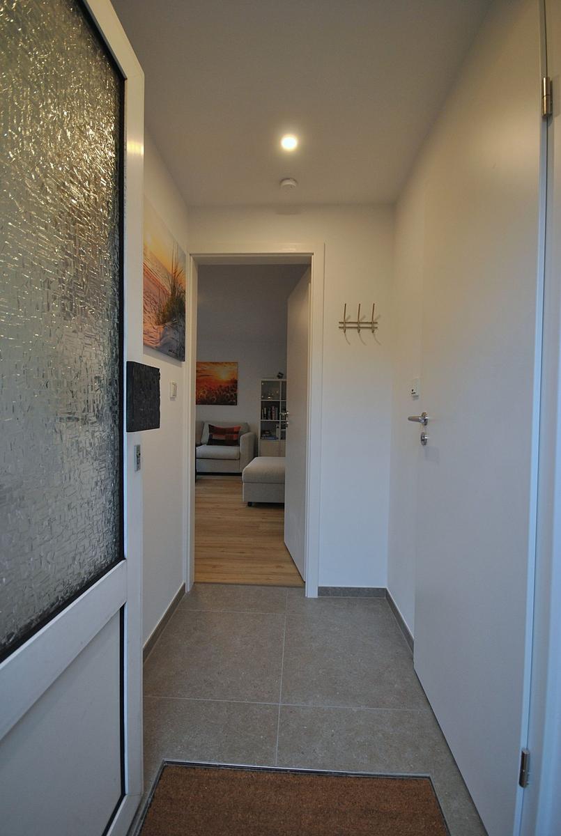 Flur mit Tür, Teppich und Blick in Wohnzimmer mit Sofa und Wandbild.