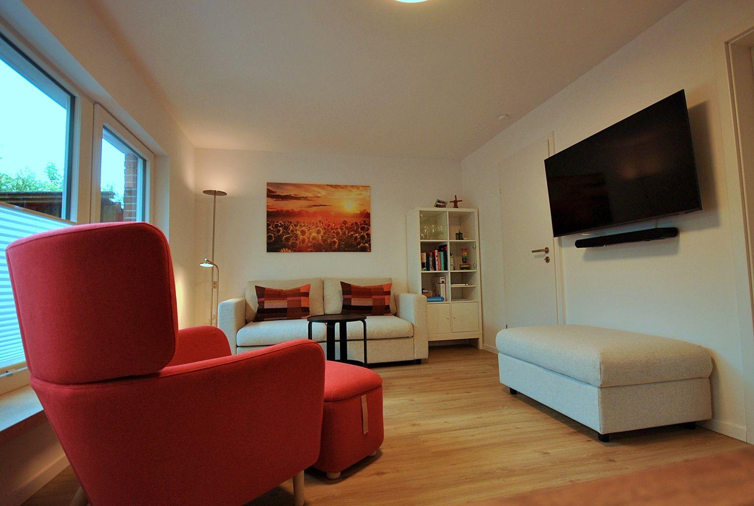 Ein Wohnzimmer mit rotem Sessel, Sofa, Fernseher und Wandbild.