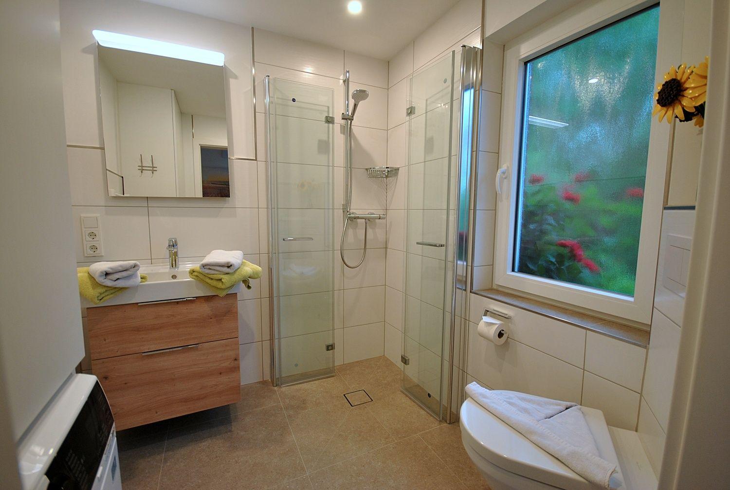 Badezimmer mit Dusche, Waschbecken und Toilette. Fenster mit Blumenmotiv.