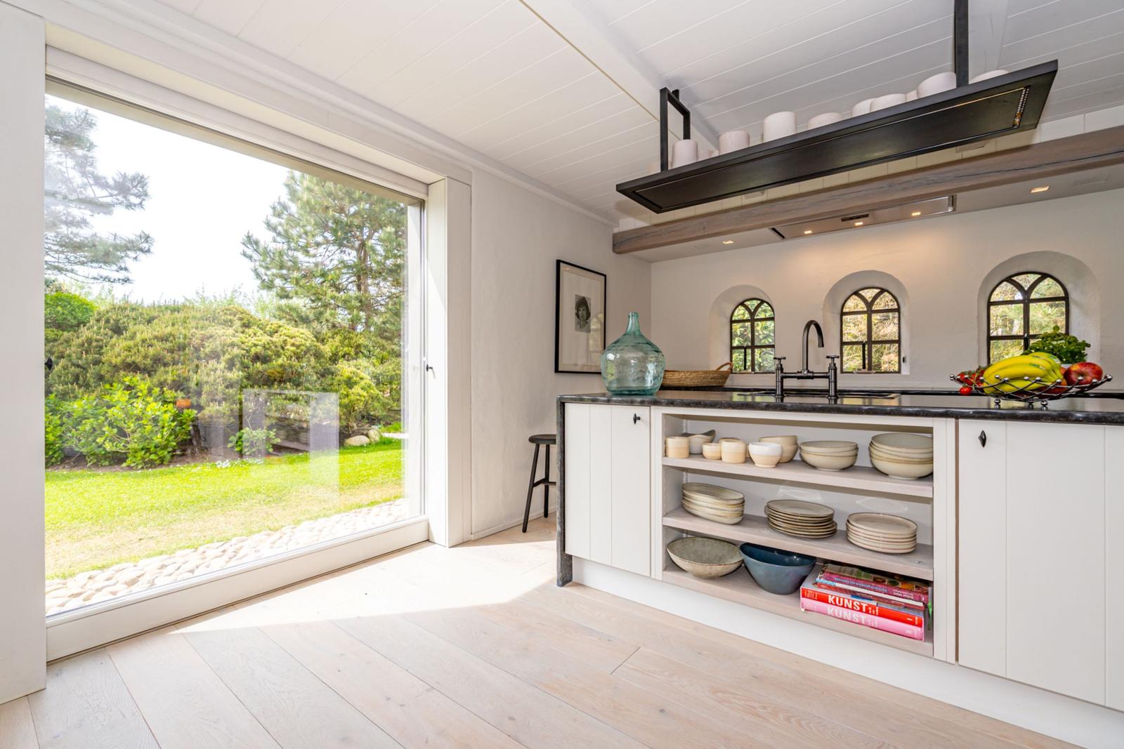 Küche mit Blick auf Garten, weiße Schränke, offene Regale und drei Bogenfenster.