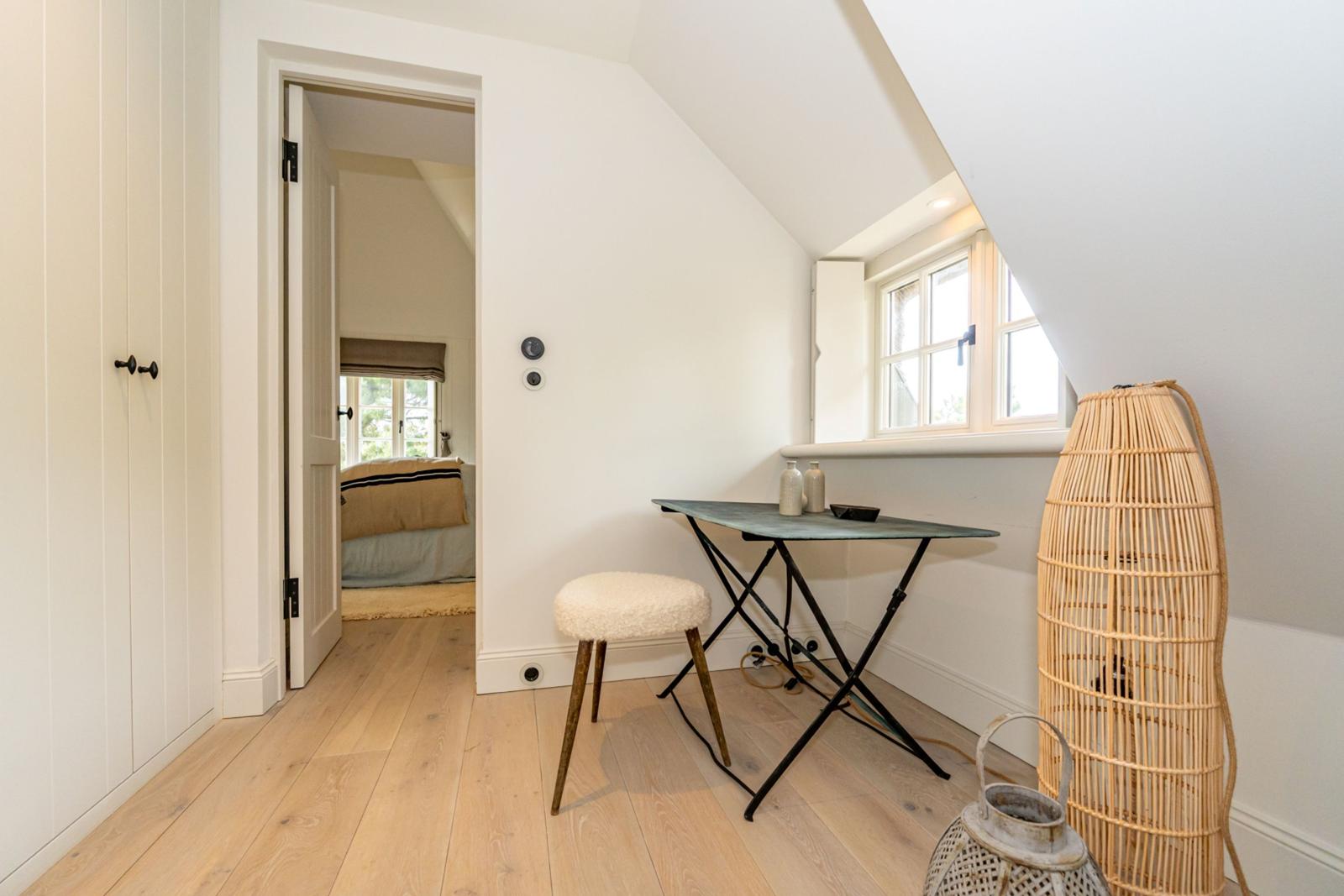 Dachgeschosszimmer mit Schreibtisch, Stuhl und Fenster. Tür führt in Schlafzimmer.