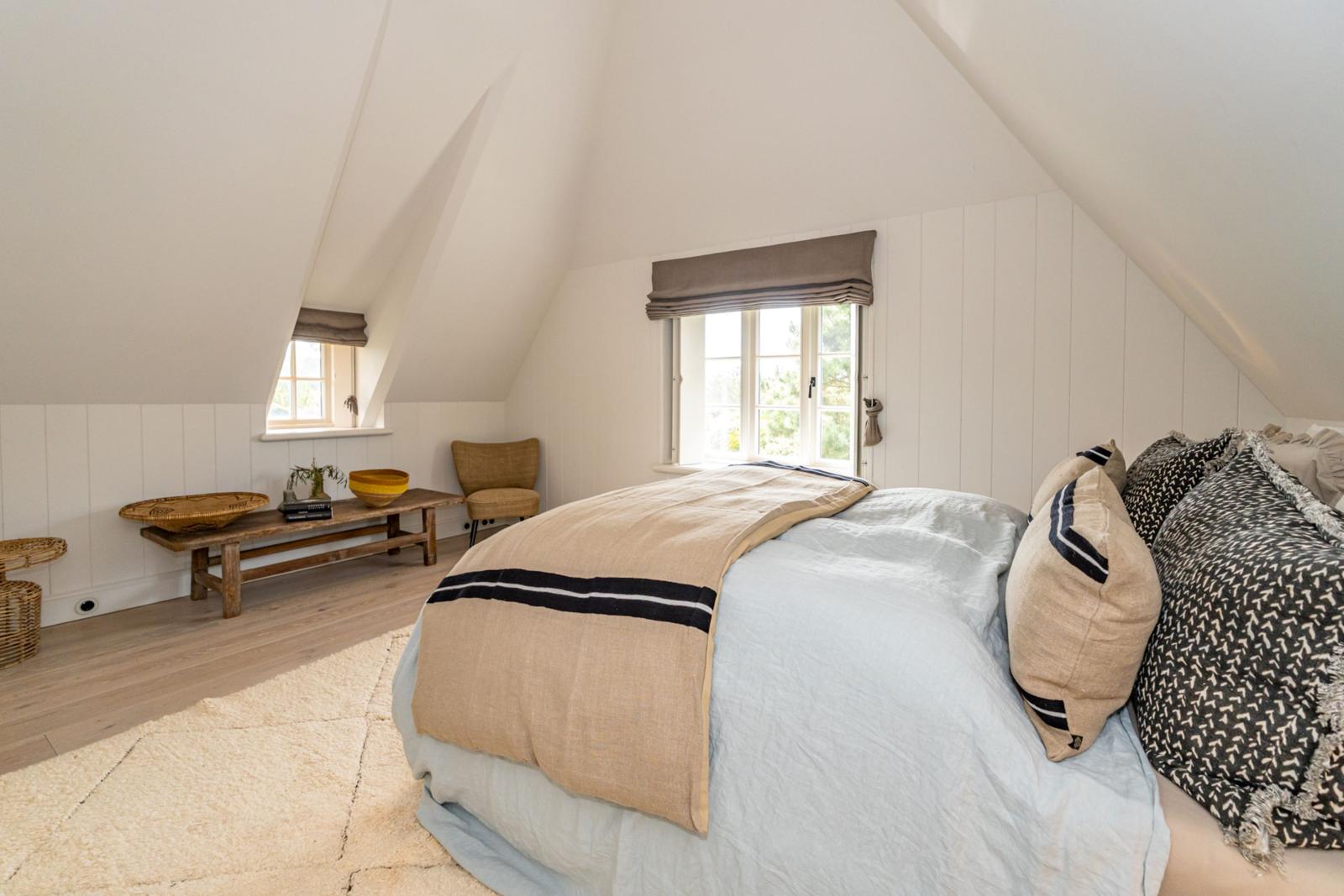 Schlafzimmer mit Dachschrägen, Bett, Fenster und Holzboden.