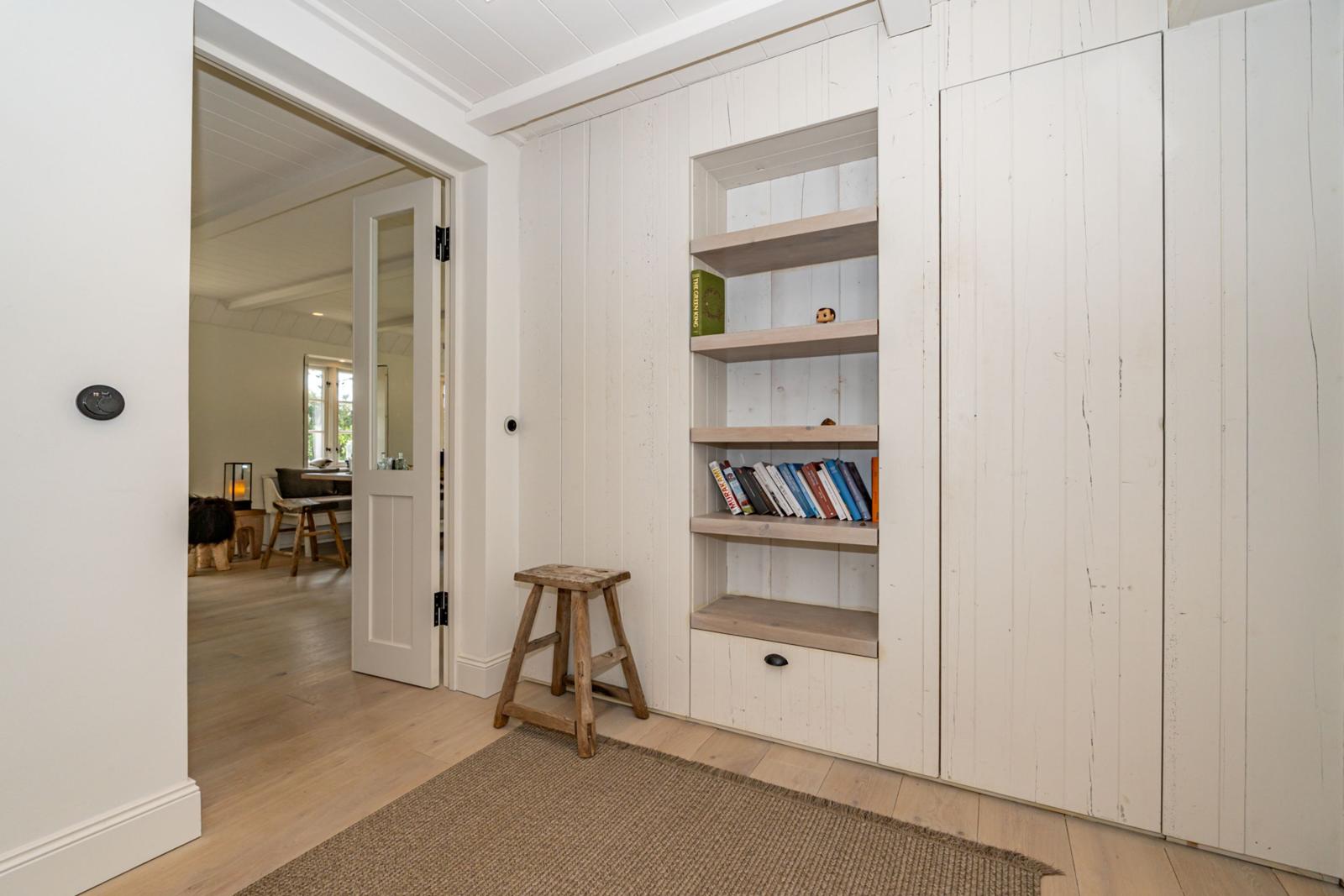 Eingangsbereich mit Bücherregal und Holzstuhl. Durchgang zu Wohnzimmer mit Tisch und Stühlen.