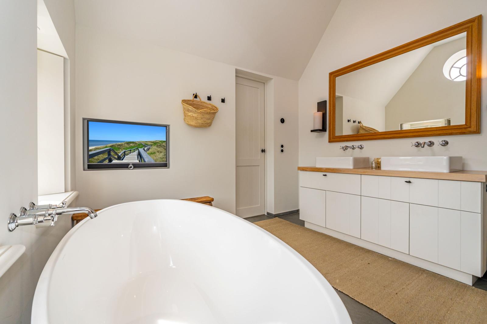 Badezimmer mit freistehender Badewanne, Doppelwaschbecken und Fernseher an der Wand.