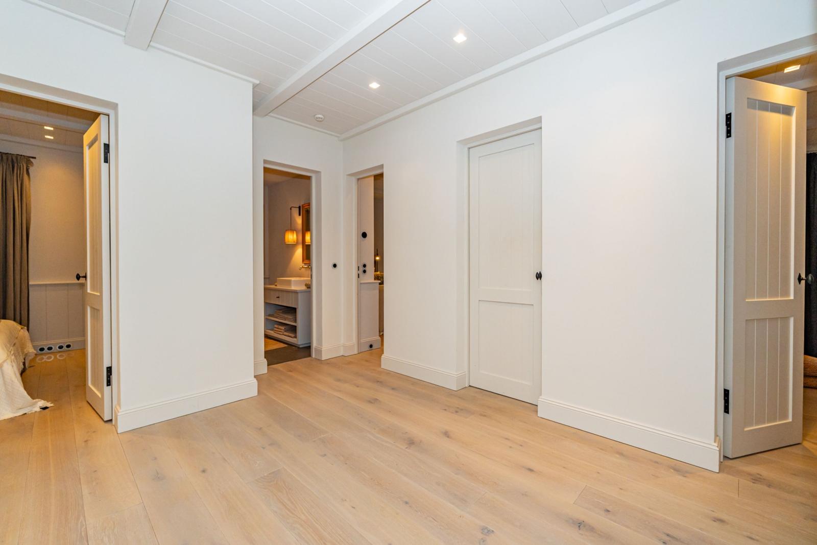 Flur mit hellen Wänden, Holzboden und Türen zu Schlaf- und Badezimmer.