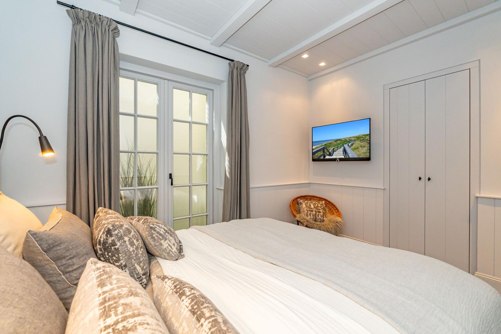 Schlafzimmer mit Bett, TV und Fenster. Wand und Decke weiß. Vorhänge grau.