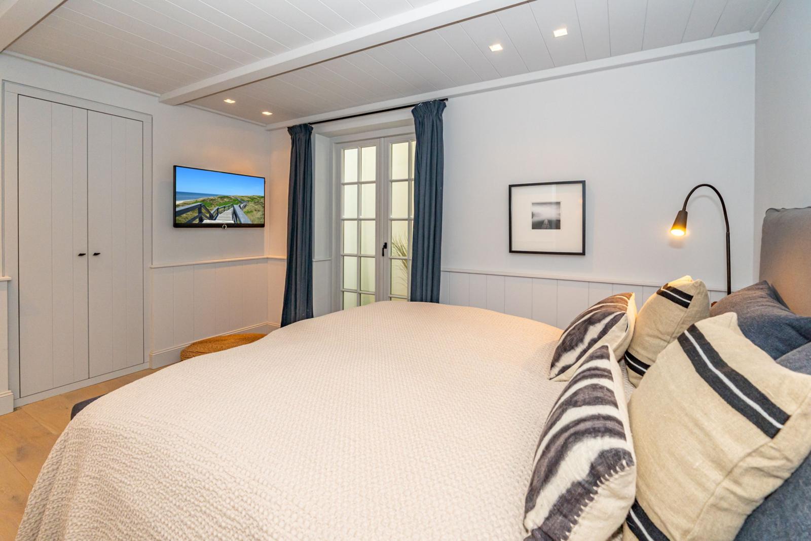 Schlafzimmer mit Bett, Fernseher und Fenster mit Vorhängen.