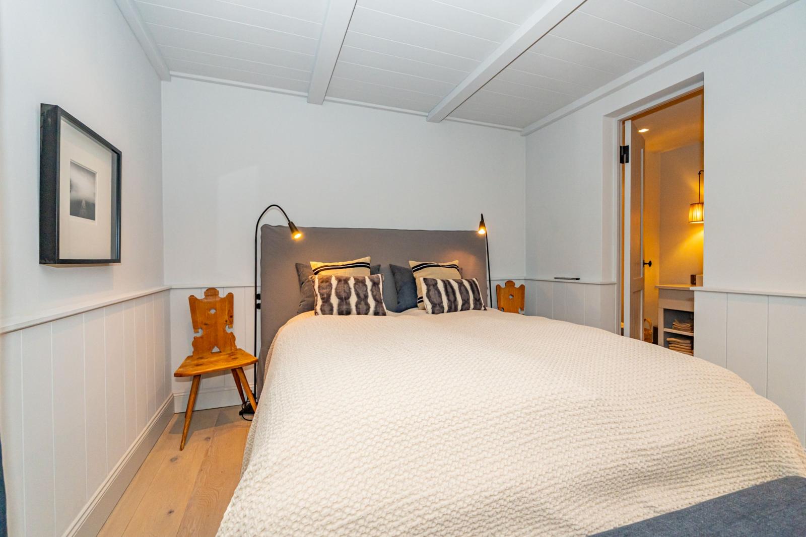 Schlafzimmer mit Bett, zwei Nachttischen und Wandbild. Hölzerne Bodenplanken und weiße Wände.
