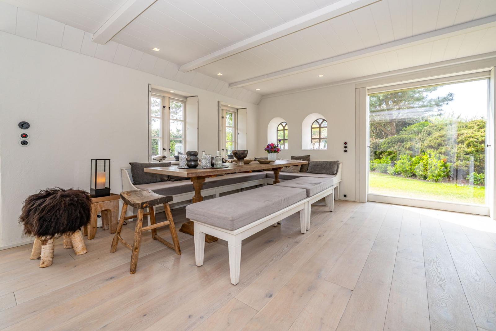 Esszimmer mit Holztisch, Sitzbänken und großem Fenster zur Gartenansicht.