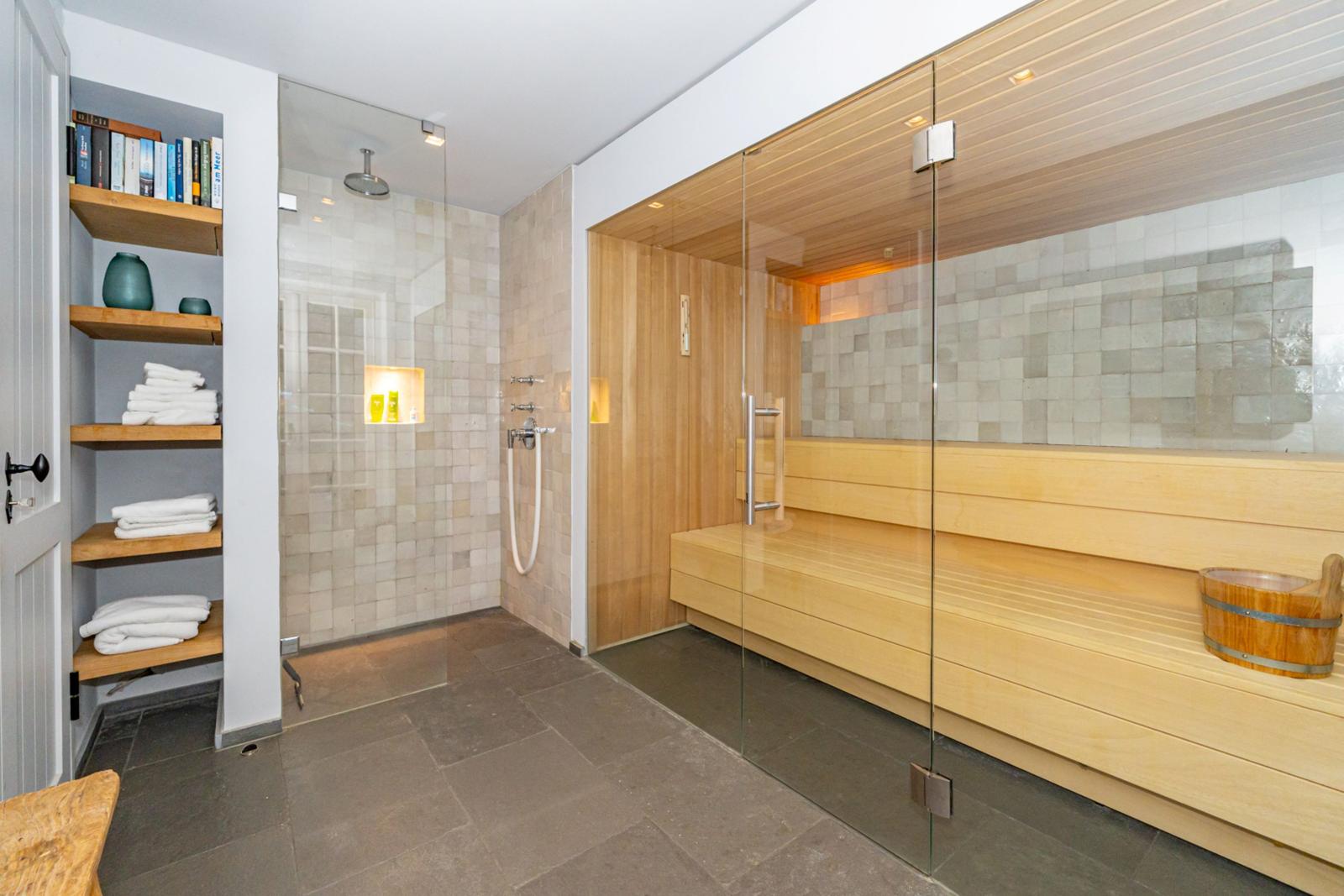 Dusche mit Glaswand, Sauna mit Holzbank und Eingangsbereich mit Regalen.
