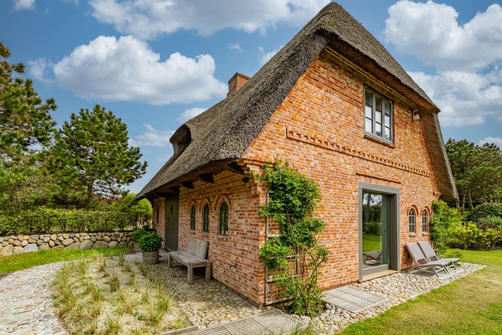 Rotes Backsteinhaus mit Strohdach, Gartenbereich und Holzbänken.