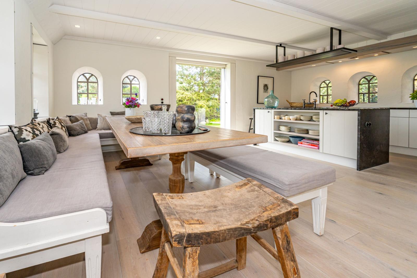Großer Essbereich mit Holztisch, Bank und Sofa. Küche mit Arbeitsplatte und Fenstern.