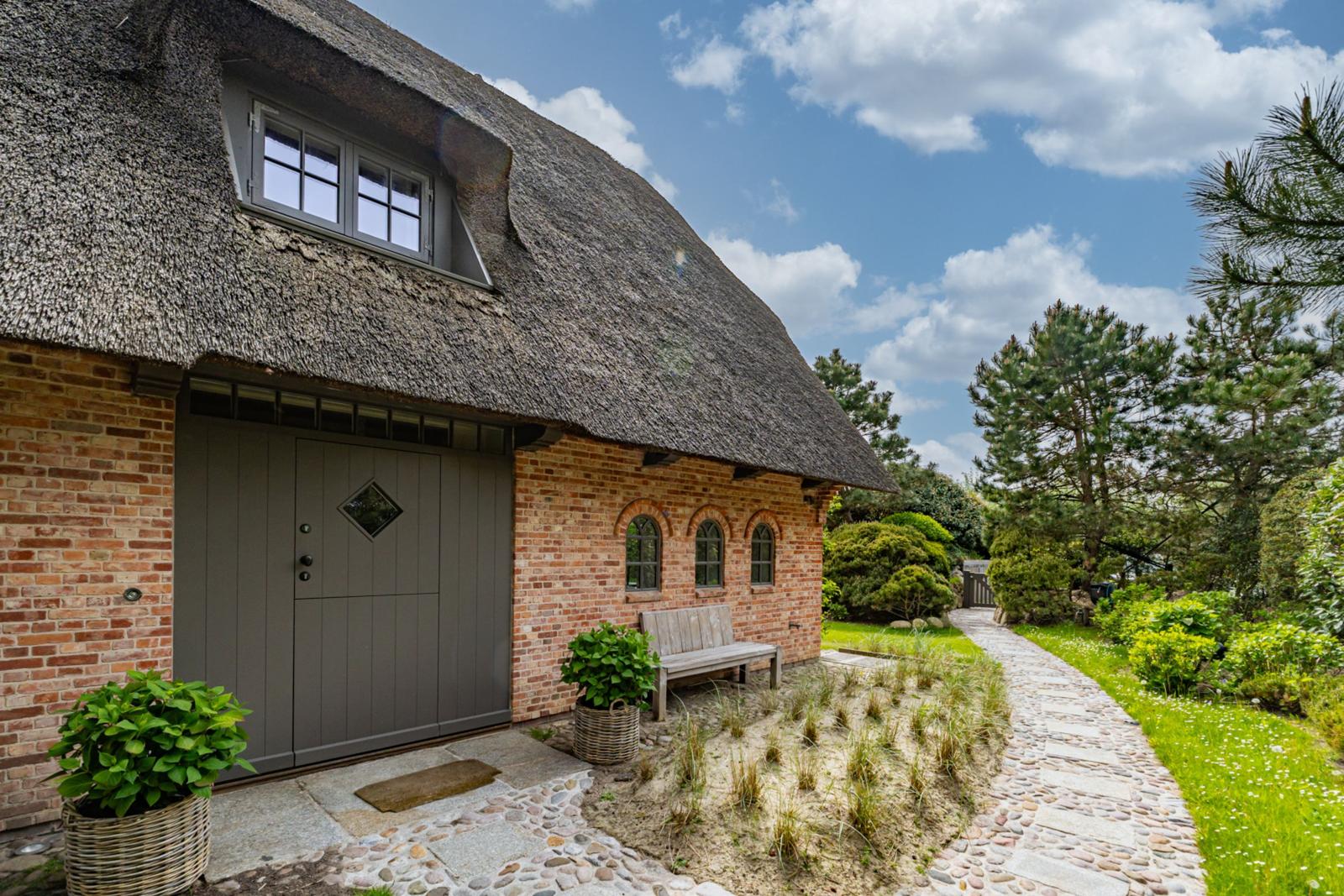 Haus mit Strohdach, Backsteinfassade und Holzbank im Garten.