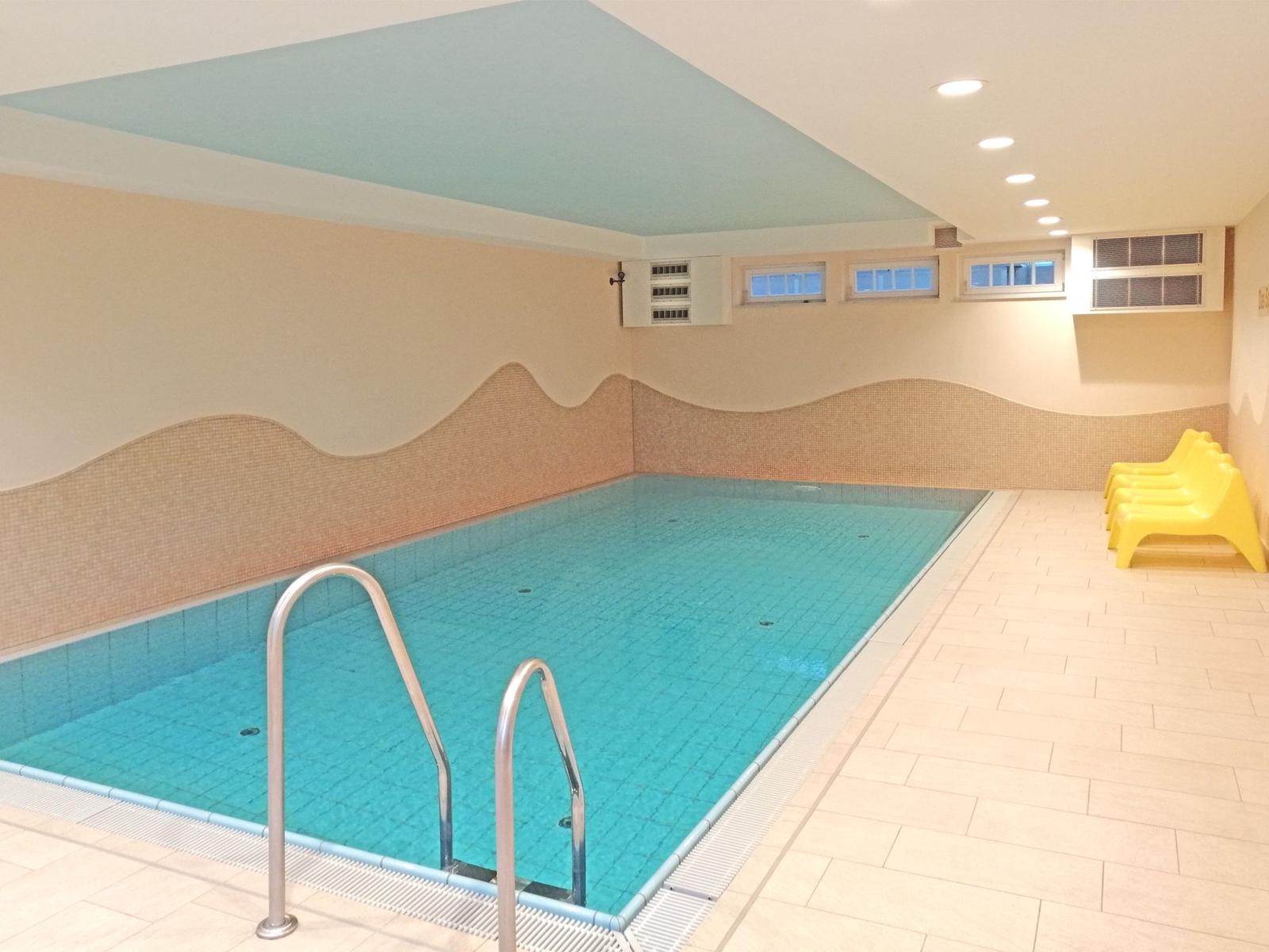 Innere Schwimmbad mit Pool, Geländer und gelben Liegestühlen an der Wand.