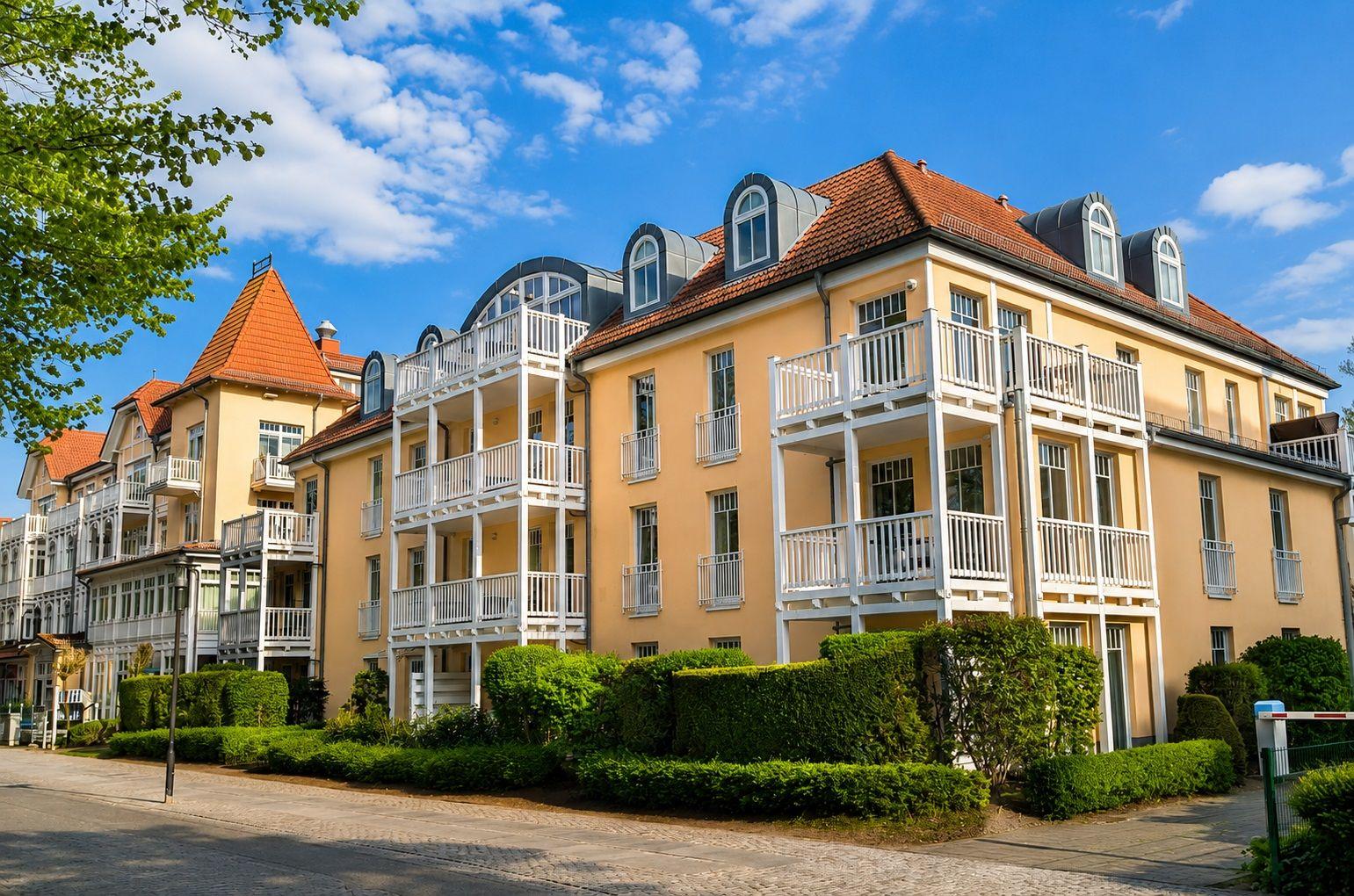 Fassade eines mehrstöckigen Wohngebäudes mit weißen Balkonen und rotem Dach.