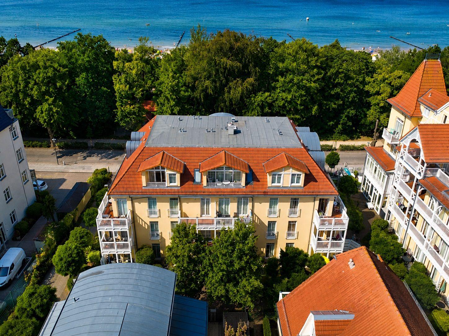 Haus mit rotem Dach und Balkonen, umgeben von Bäumen und Strand.